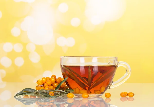 Plody rakytníku a šálek čaje na žlutém pozadí abstraktní. — Stock fotografie