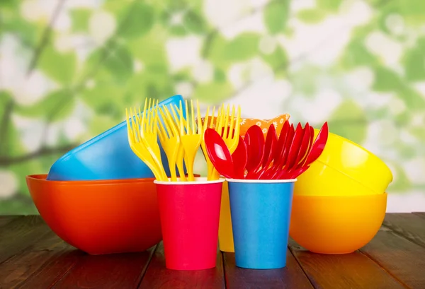 Цветная пластиковая посуда: миски, вилки, ложки на абстрактном зеленом  . — стоковое фото