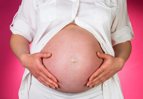 Kobieta w ciąży jest głaskanie brzucha z rąk na różowym tle. — Zdjęcie stockowe