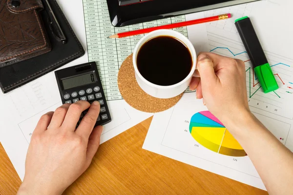 Miniräknare och kopp kaffe i handen på bakgrund av skrivbordet. — Stockfoto