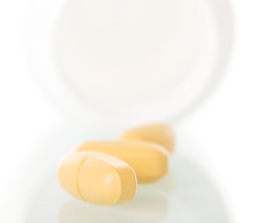 Beyaz arka plan üzerinde izole şişe dökülen sarı haplar.