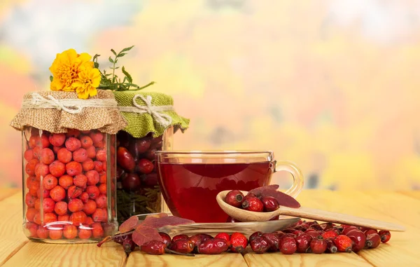 En frascos de vidrio bayas de rowan, rosa silvestre y té taza . — Foto de Stock