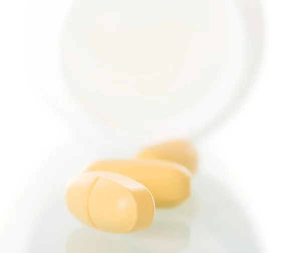 Yellow pills spilled from  bottle isolated on  white background.