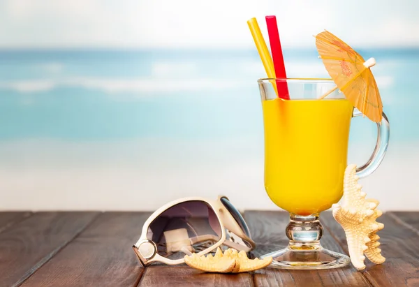 Vaso de zumo de naranja y gafas de sol en la playa . — Foto de Stock