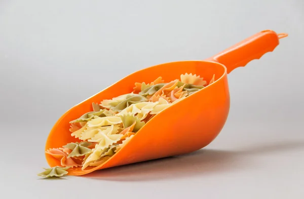 Orange scoop Farfalle pasta på ljus grå bakgrund. — Stockfoto