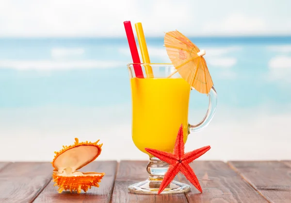 Oranje cocktail, zeesterren en kistje met pearl op blauwe zee. — Stockfoto