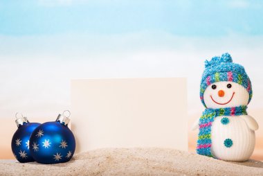 Boş beyaz kartpostal, kardan adam, Noel topları kum onseashore.