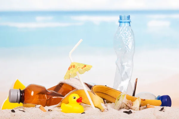 Garrafas de plástico, resíduos alimentares, pato de borracha na areia contra o mar . — Fotografia de Stock