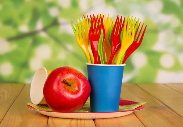 Bright disposable tableware and apple on  abstract green background. — Stock Photo, Image