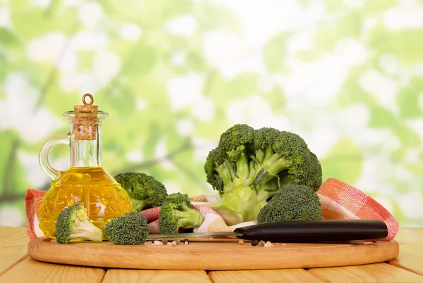 Broccoli freschi, olio in bottiglia, spezie, coltello, asciugamano su astratto verde  . — Foto Stock