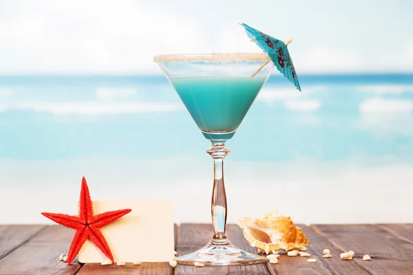 Carta bianca, cocktail, stelle marine e conchiglie in sabbia contro il mare . — Foto Stock