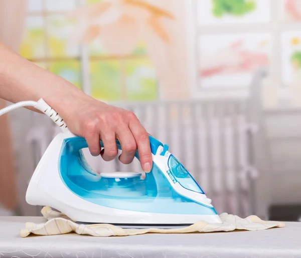 Womans mão acariciando roupas vapor ferro na sala de fundo . — Fotografia de Stock