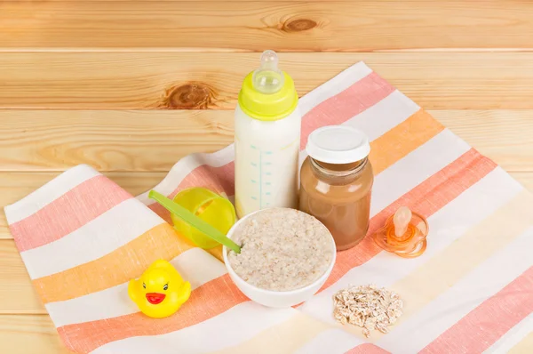 Bottle of milk, oatmeal, mashed potatoes,  nipple on  light wood. — Stock Photo, Image