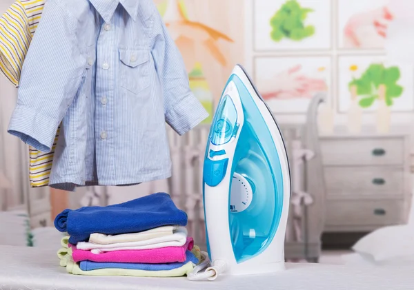 Steam iron and clothes on  background of  childs room.