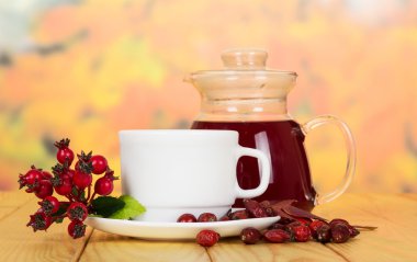 Sürahi ve bardak çay kuşburnu çilek arka plan sonbahar yaprakları üzerinde.