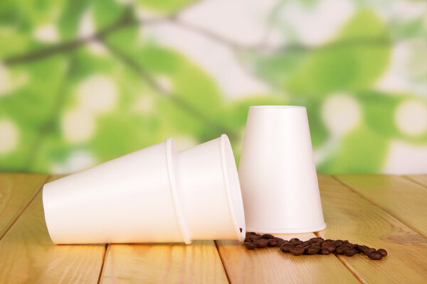 Disposable paper cups and coffee beans on  abstract green background.