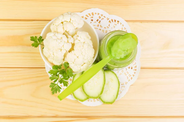 Jar baby puree bloemkool, courgette op achtergrond licht hout. — Stockfoto