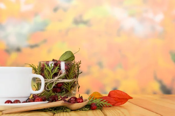 Kalça, çay bardağı ve tahta kaşık arka plan sonbahar yaprakları üzerinde. — Stok fotoğraf
