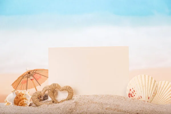 Tarjeta en blanco con conchas de mar, corazones en arena en la playa . — Foto de Stock