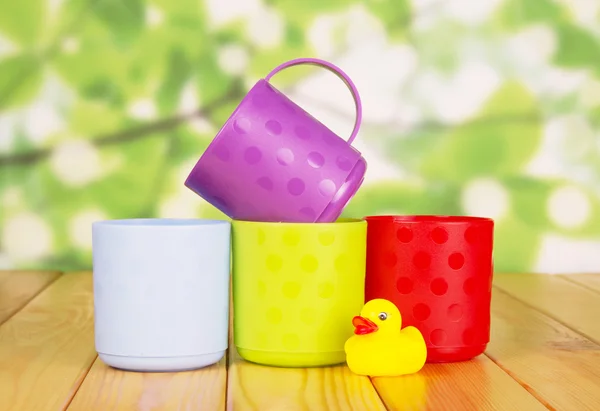 Colorful plastic cups and rubber duck on  green abstract background. — Stock Photo, Image
