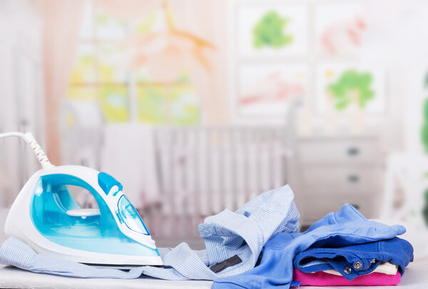Steam iron, ironing board and clothes on  background of  room.