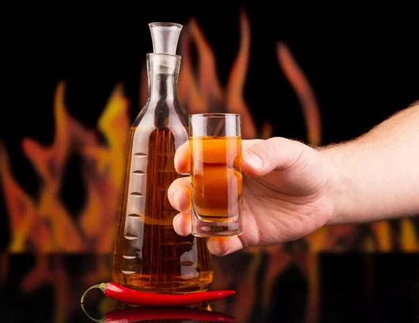 Bottle, glass pepper vodka in hand on background  flames. — Stock Photo, Image