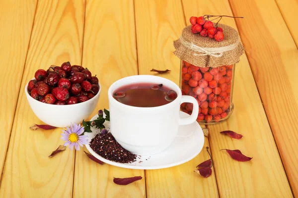 Hips, mountain ash and  cup  tea on  background light wood. — Stock Photo, Image