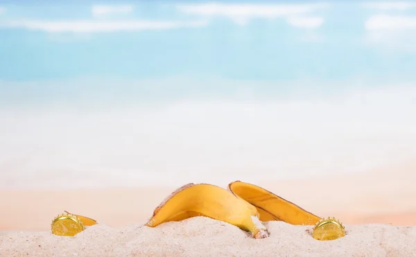 Banana peel and plug in  sand against the sea. — Stock Photo, Image