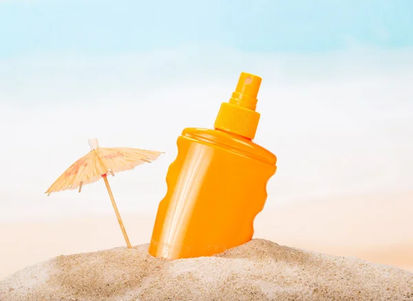 Flaska av solskyddsmedel i sanden mot havet. — Stockfoto