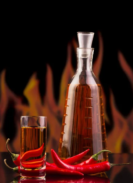 Botella, vodka de vidrio, chile rojo picante sobre llamas de fondo . — Foto de Stock