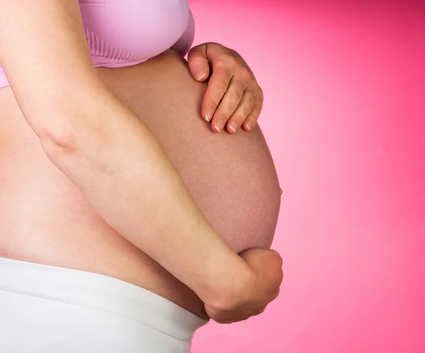Femme enceinte avec les mains sur le ventre, fond rose . — Photo