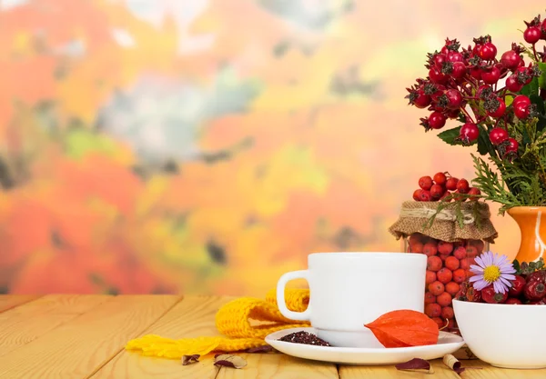 Rosa mosqueta, bayas de rowan, taza de té en el fondo hojas de otoño . —  Fotos de Stock