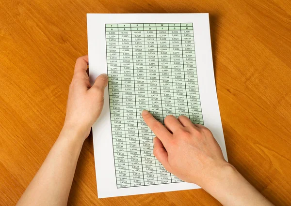 Female hand holding  sheet with calculations on background  wooden table. — Stock Photo, Image