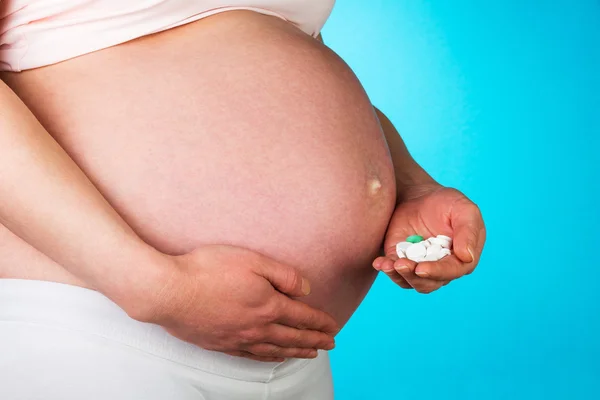 Mujer embarazada sosteniendo en la mano píldoras vitamínicas sobre fondo azul . — Foto de Stock