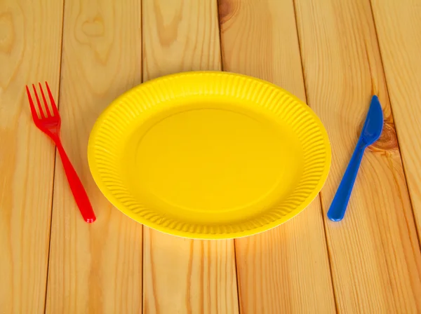 Piastre monouso gialle, coltello e forchetta in plastica su legno chiaro — Foto Stock