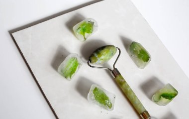 El ele tutuşan yeşil yüz silindiri ve buz küpleri. Cilt bakımı için cilt silindiri.