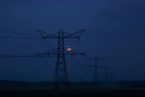 黄昏时分 黄昏时分 月亮把橙色的红色映入眼帘 电塔映衬在平坦的农田上 — 图库照片