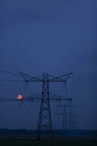 在平坦的农田里 蓝色的黄昏黄昏时分 月亮在电塔的左边把橙色的红色映入眼帘 — 图库照片