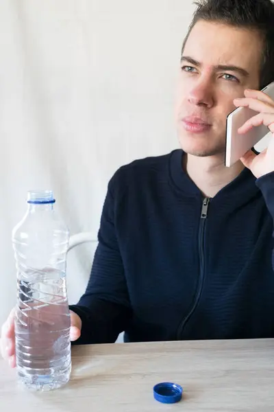Adolescente Sentado Sosteniendo Una Botella Agua Mientras Habla Por Teléfono — Foto de Stock