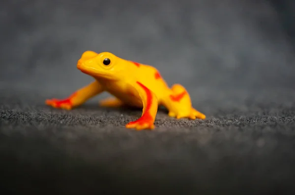 A closeup of a toy figurine of a yellow frog with red stripes