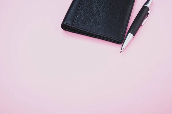 一支滚珠笔的特写 在一个小皮夹旁边 夹在浅粉色的背景上 — 图库照片