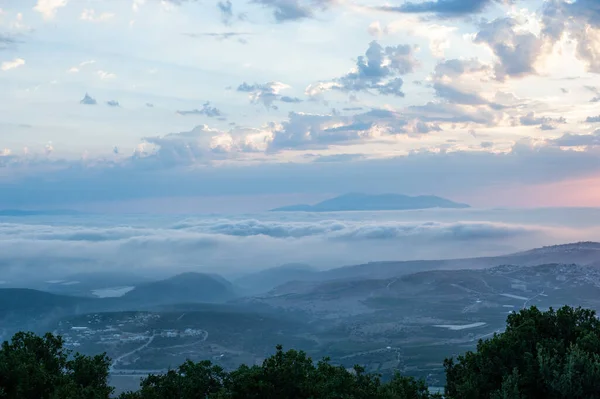 Wide shot of mountains at sunrise, with clouds below and above, shot from Meron mountain in Israel