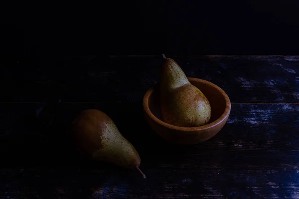 木の鉢の中に梨が2つあり もう1つは暗闇の中にあります — ストック写真