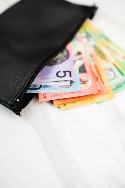 a vertical shot of Australian dollar banknotes in a black wallet on the white background