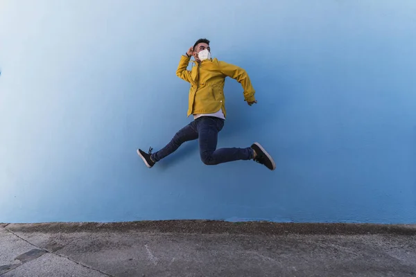Młody Mężczyzna Żółtej Kurtce Masce Skaczący Pod Ścianą — Zdjęcie stockowe