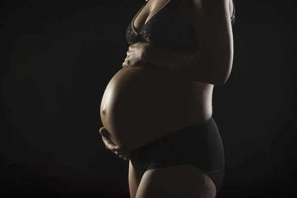 一个怀孕的女人抱着婴儿颠簸 穿着深色背景的黑色内衣 — 图库照片