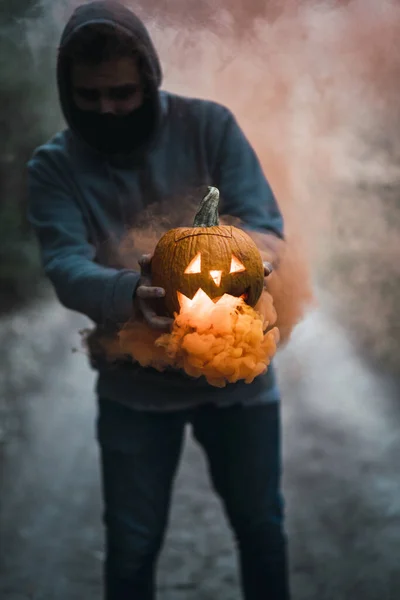 Pionowe Ujęcie Człowieka Trzymającego Rzeźbioną Dynię Pomarańczowym Dymem Koncepcja Halloween — Zdjęcie stockowe