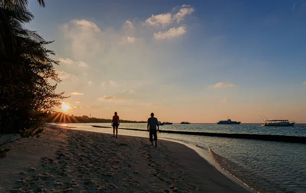 日の出の間に海に囲まれたビーチを歩いている2人 — ストック写真