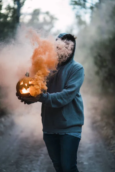 Pionowe Ujęcie Człowieka Trzymającego Rzeźbioną Dynię Pomarańczowym Dymem Koncepcja Halloween — Zdjęcie stockowe