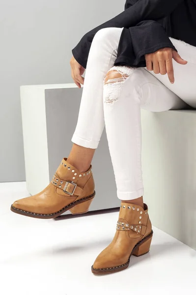 a vertical shot of a sitting female model with ripped white pants and brown shoes